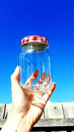 Cropped hand holding glass jar against clear blue sky