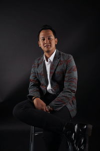 Portrait of young man sitting against black background