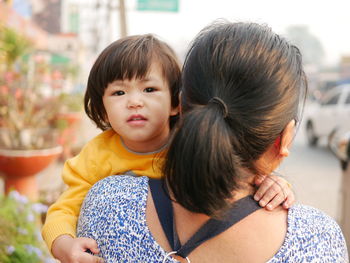 Mother carrying daughter on road in city