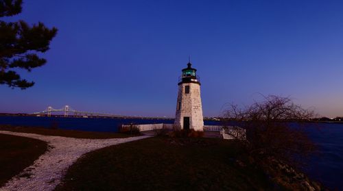 Lighthouse amidst buildings and sea against clear blue sky