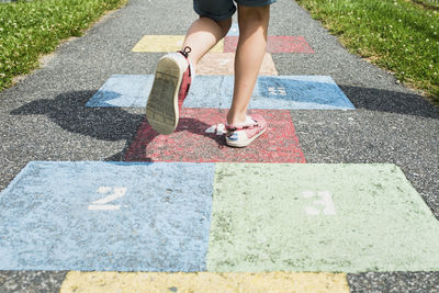 Low section of boy playing hopscotch on road