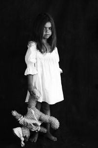 Portrait of girl with toy standing against black background