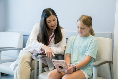 Pediatrician looking at girl using tablet computer in hospital