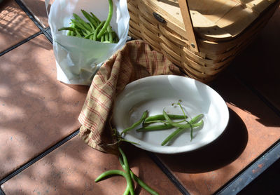 High angle view of green peas by wicker basket on table