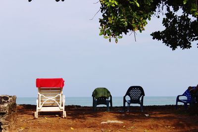 Empty chairs on beach against clear sky