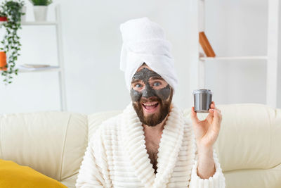 Portrait of young man applying facial mask at home