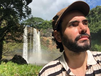 Man in cap looking away against waterfall