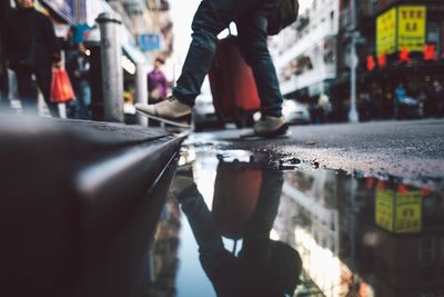 Low section of man standing by puddle on street