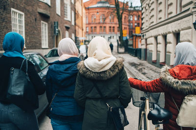 Rear view of female friends walking with bicycle on street in city