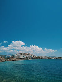 Scenic view of sea by buildings against blue sky