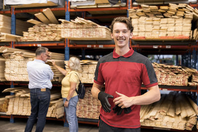 Portrait of smiling salesman holding glove while standing in front of rack at hardware store