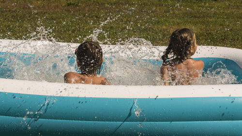 Rear view of playful siblings in wading pool at lawn