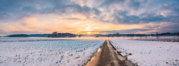 Landscape panorama with road, white fields cover by snow and sunset sky.