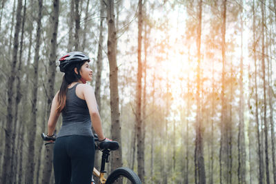 Low angle view of female cyclist standing with bicycle in forest