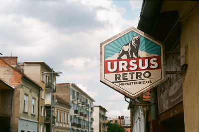 Low angle view of road sign by buildings against sky