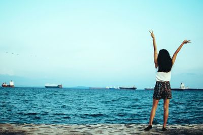 Rear view of woman gesturing peace signs while standing at sea shore