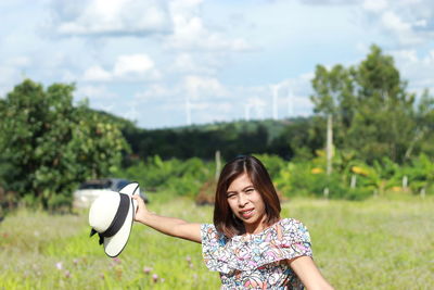 Portrait of woman holding hat while standing on field