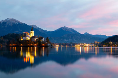 Scenic view of lake by illuminated buildings against sky