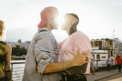 Side view of romantic gay man kissing non-binary friend on promenade