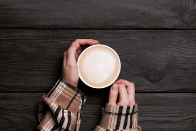 Woman hands holding morning cup of coffee on vintage wooden table top view. cozy fall breakfast.