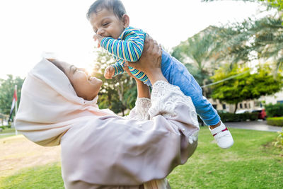 Side view of mother holding son mid-air at park