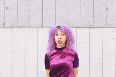 Woman with purple hair blowing bubble gum standing against wall