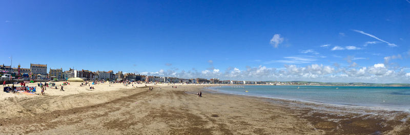Panoramic view of people on beach against blue sky