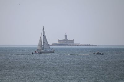 Boats in sea with lighthouse against sky