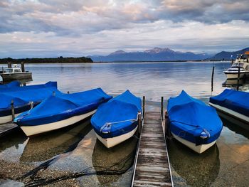 Boats moored on pier at lake against sky