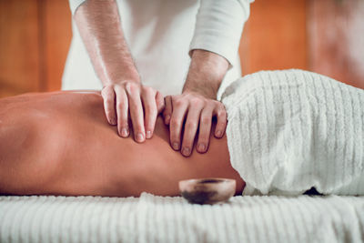 Midsection of male massage therapist massaging shirtless female customer in spa