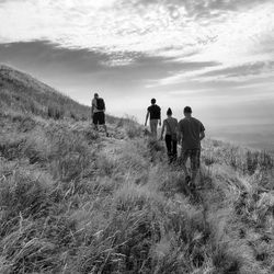 People standing on grassy field against cloudy sky