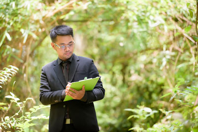 Young man with arms outstretched standing against plants