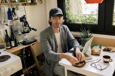 High angle view of male architect eating snacks while sitting at desk in home office