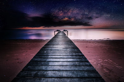 Pier over lake against sky at night