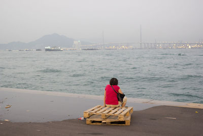 Rear view of woman sitting on wooden pallet at beach