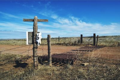 Cross on wooden post on road against sky