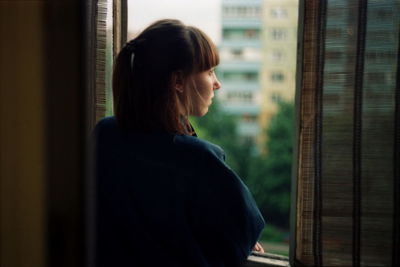 Young woman looking through window at home