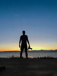 Silhouette man standing on shore against blue sky