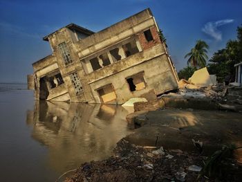 Old building against sky broken in river bank for climate change 