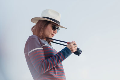 Side view of woman holding camera against sky