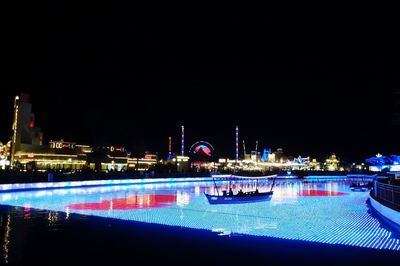 Illuminated buildings by river against clear sky at night