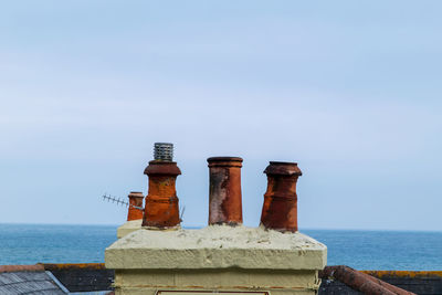 Dirty chimney stacks by sea against clear sky