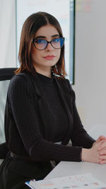 Portrait of young woman using laptop while sitting in office