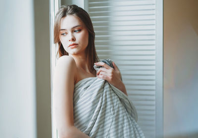 Woman wrapped in blanket looking through window at home