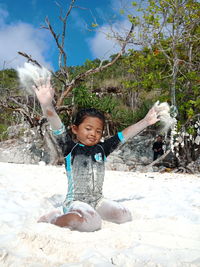 Portrait of happy girl playing with sand at beach against sky during sunny day