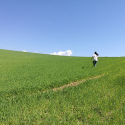 Rear view of woman running on grassy field against blue sky