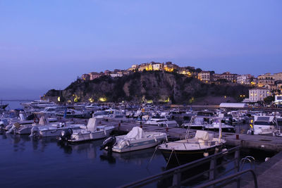 Sailboats moored in harbor against buildings in city at dusk