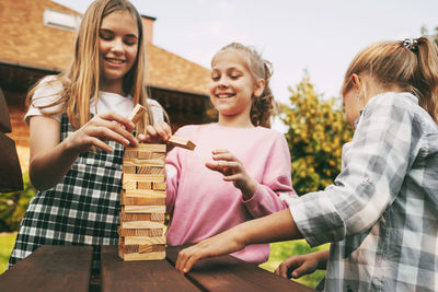 Three beautiful sisters are playing a wooden board game outdoors near their home. 