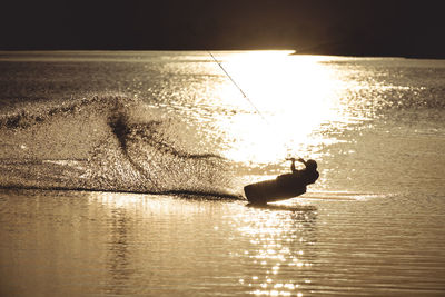 Silhouette person on sea against sky during sunset