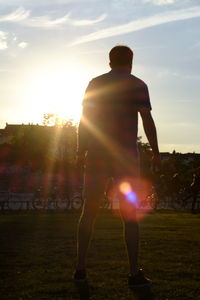 Rear view of man standing on field against sunset sky